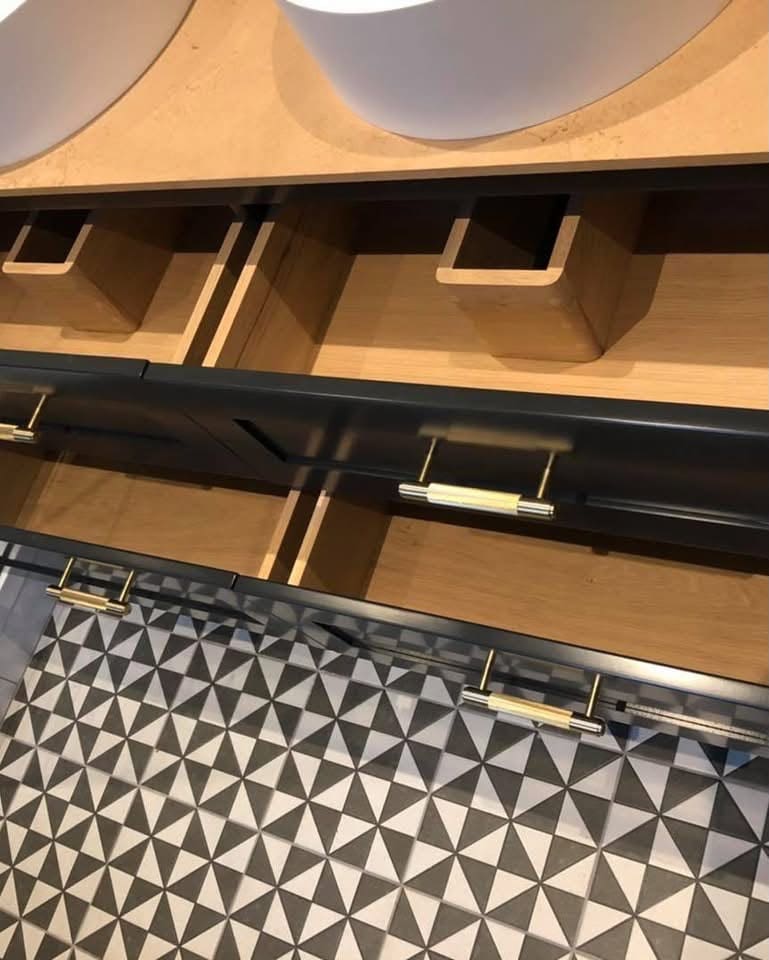 Open wooden drawers with black painted fronts and gold handles in a bespoke bathroom vanity