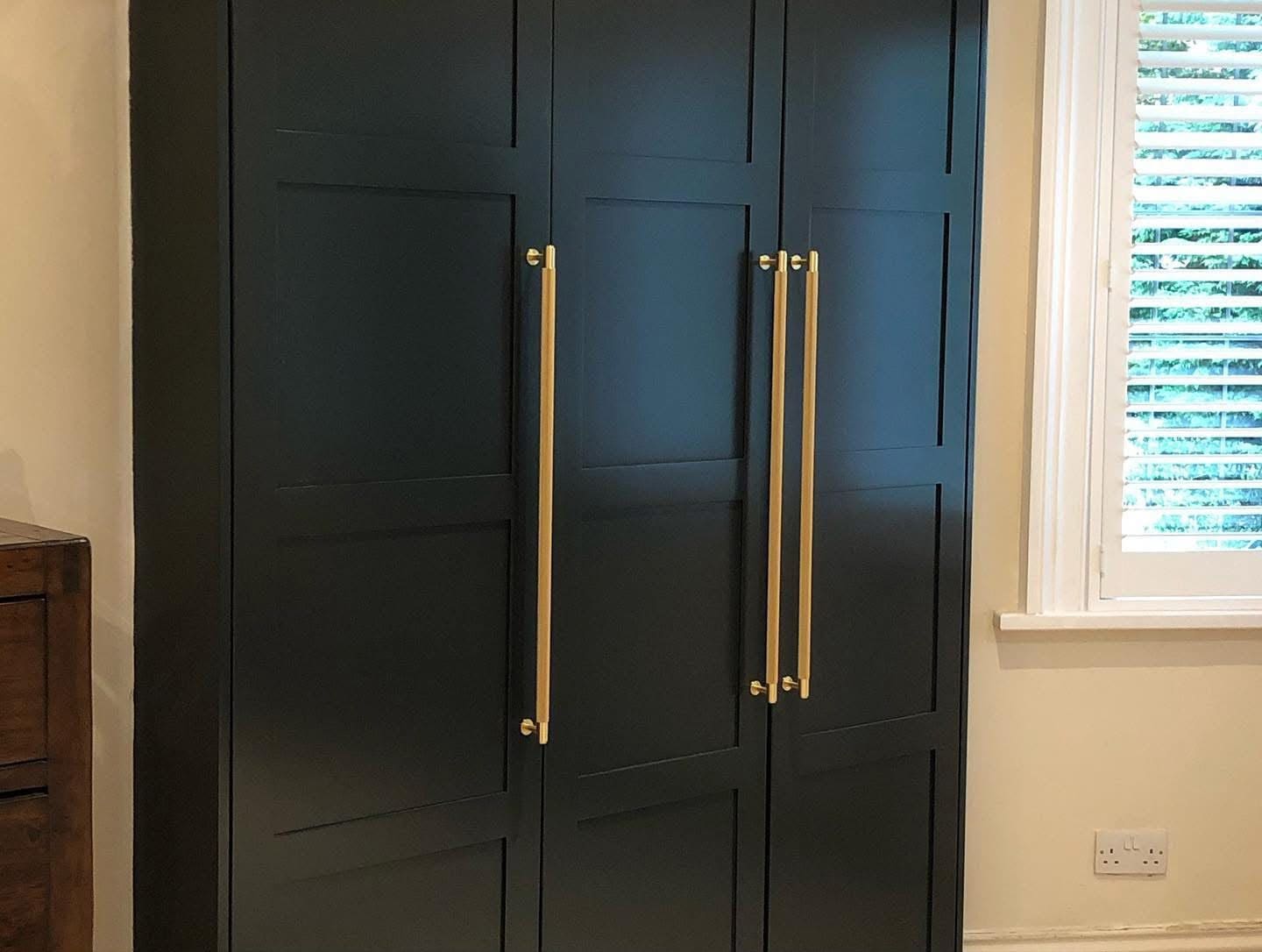 Black painted Shaker-style fitted wardrobe with gold handles in a bedroom